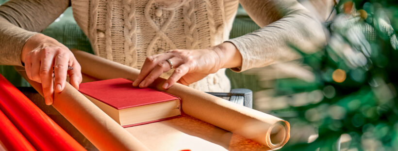 Woman wrapping a book as gift in recycled card and decorate it with dried oranges and fir branches.