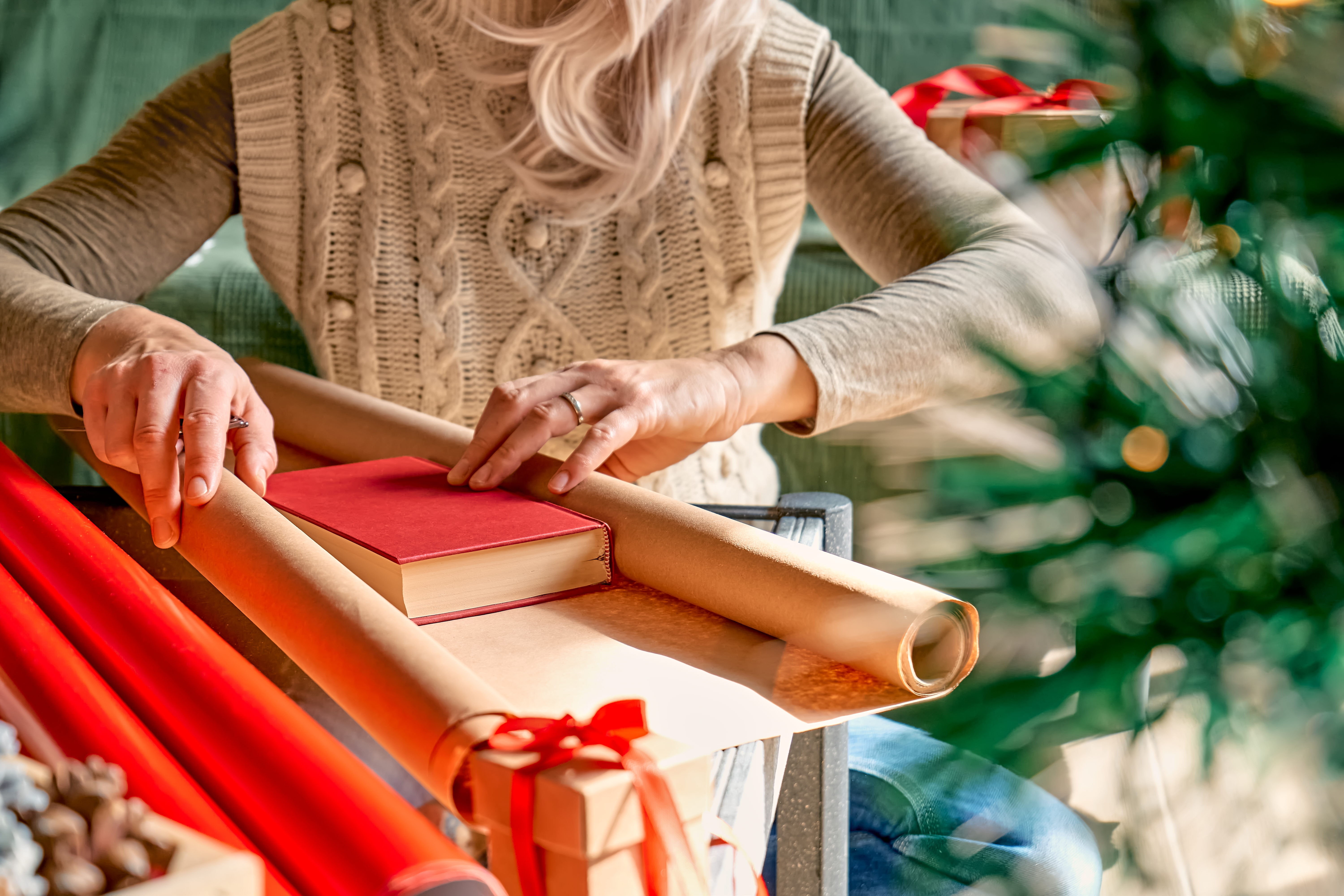Woman wrapping a book as gift in recycled card and decorate it with dried oranges and fir branches.